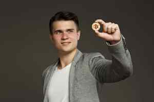 como investir em bitcoin? - homem segurando moeda física de bitcoin