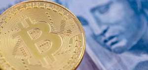 Moeda de bitcoin e nota de real lado a lado