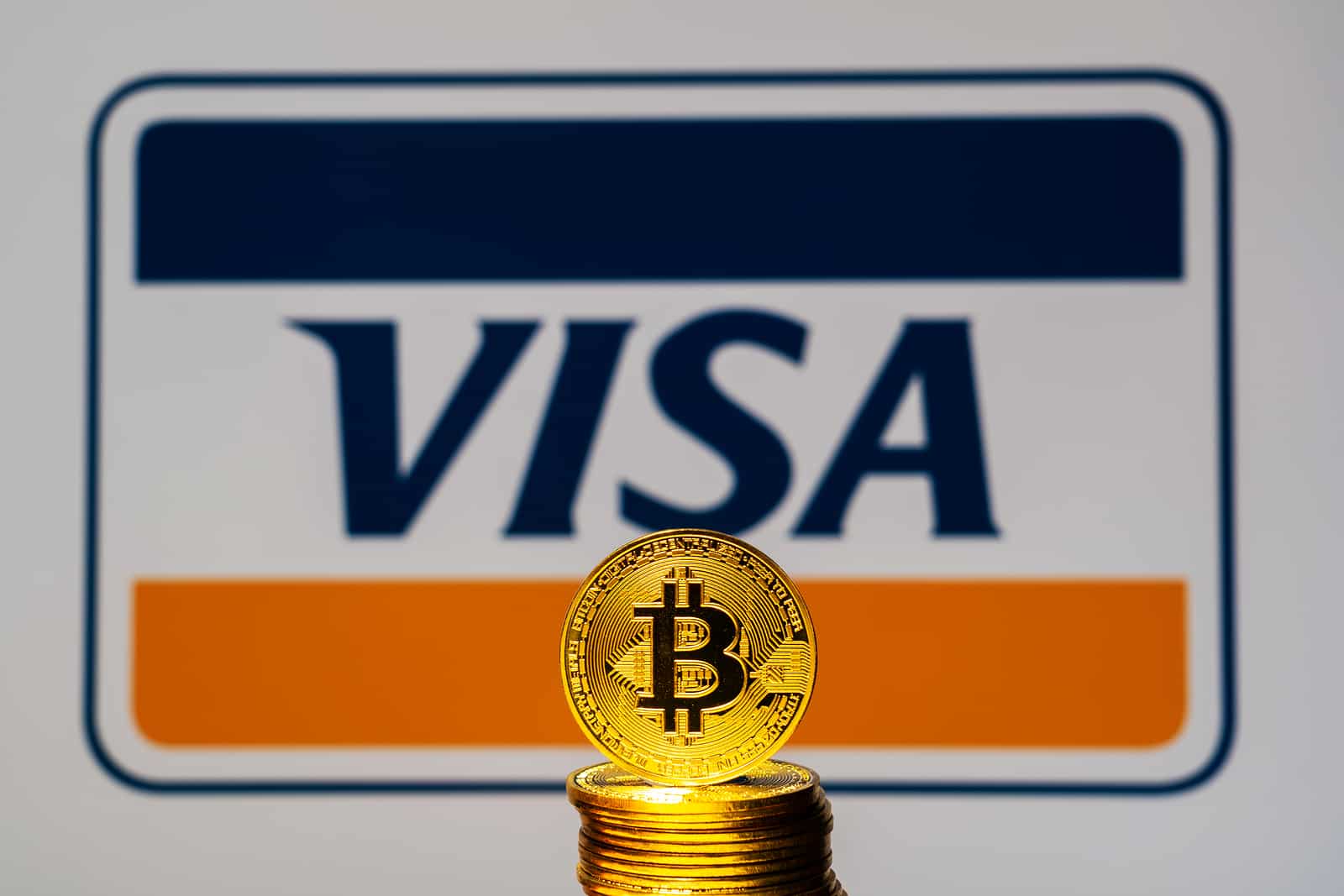 Moeda de Bitcoin e logo antigo da Visa atrás