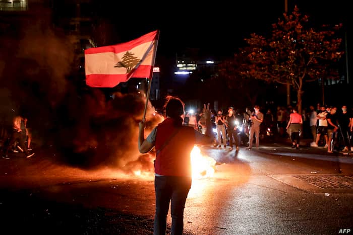 libanesa segurando a bandeira do país e fogo ao fundo