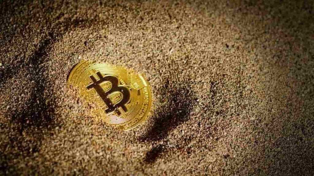 Moeda de bitcoin enterrada na areia