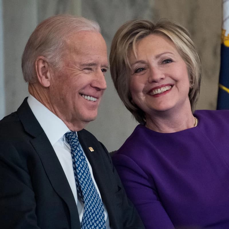 Joe Biden e Hillary Clinton sorrindo juntos. Dois viciados no poder.