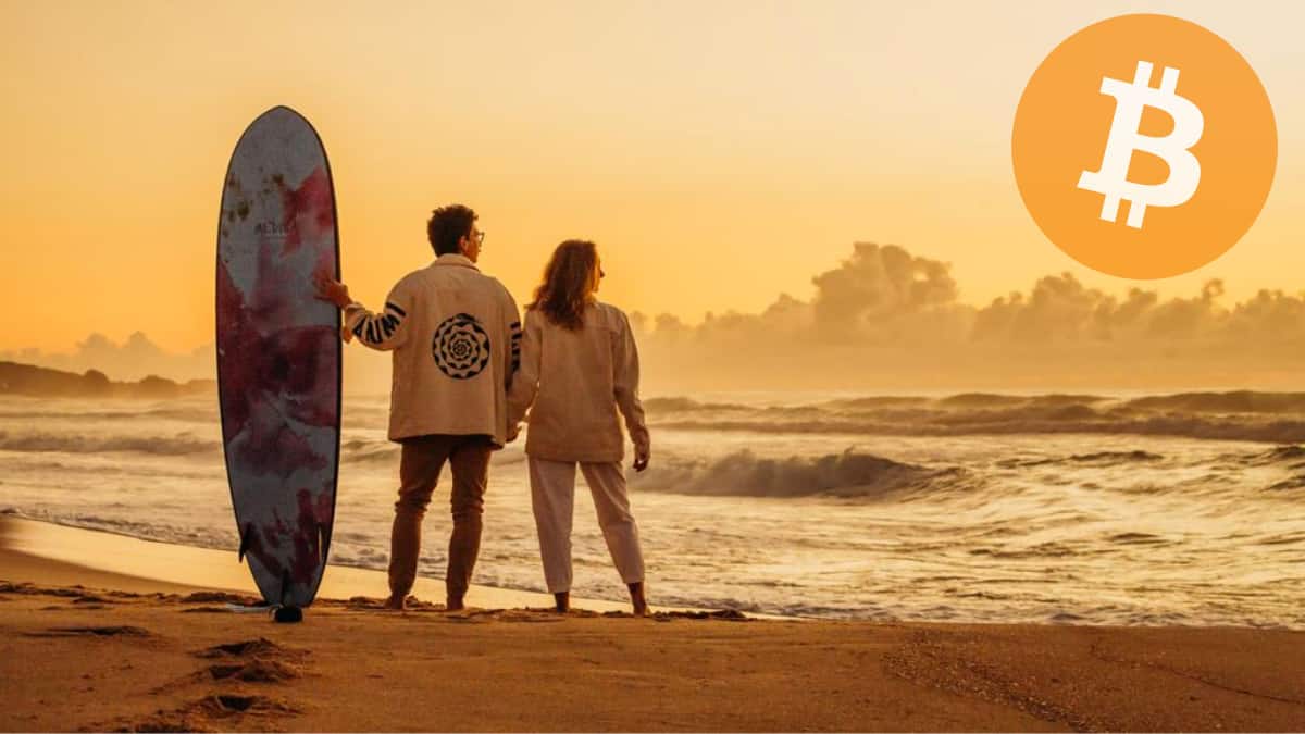 Lorenzo e Maria Fernanda na praia, com prancha de surf olhando o horizonte, com o símbolo do Bitcoin no lugar do sol. - Casal Bitcoiner