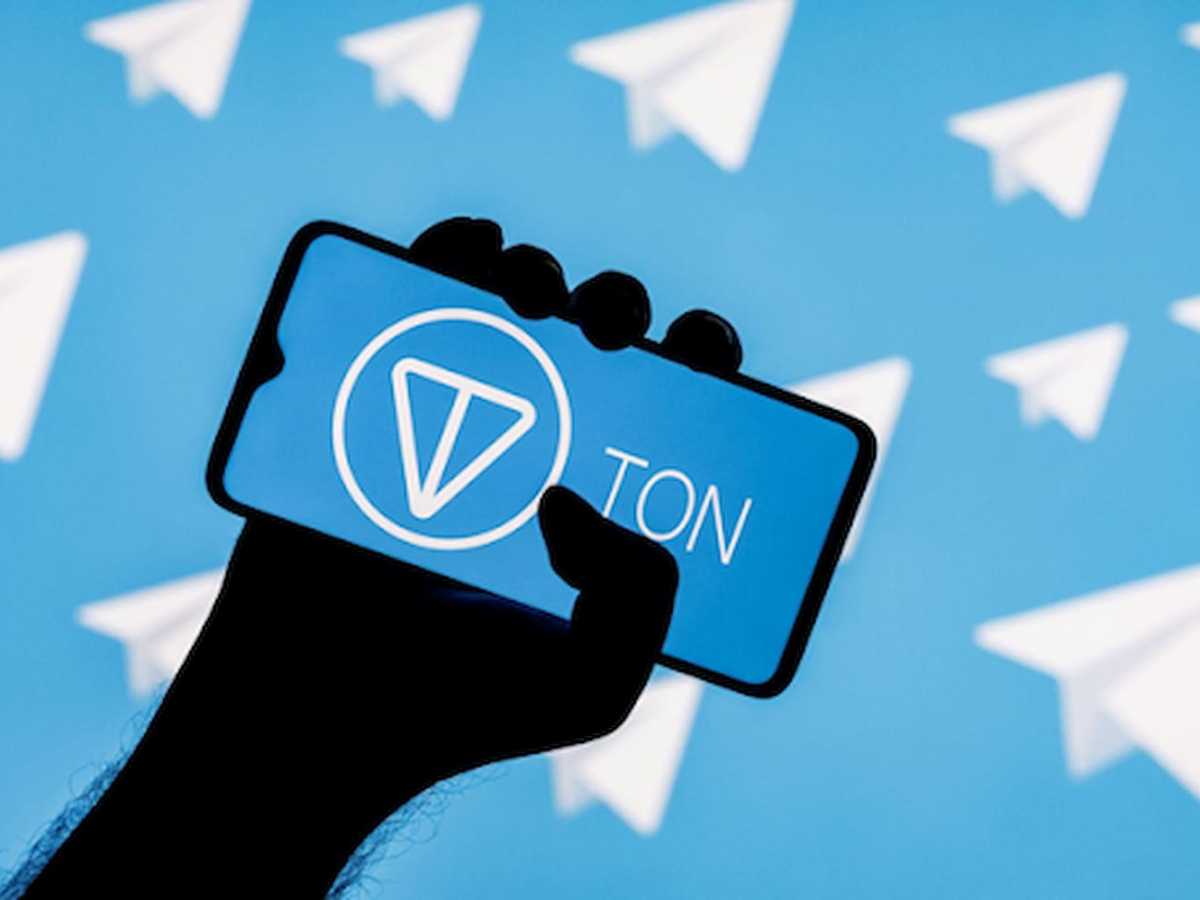 Mão segurando um celular com o logo da Toncoin